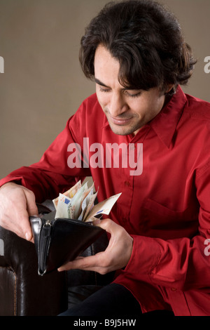 Giovane uomo che guarda il suo portafoglio completo, lieto Foto Stock