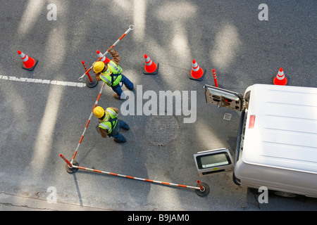 Utility di strada lavoratori tenendo le barriere che circondano un tombino. Foto Stock