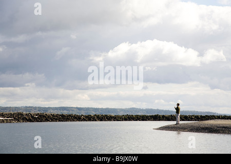 Sta un uomo con un telefono cellulare in mano in corrispondenza del bordo di un banco roccioso in prossimità del Puget Sound, Washington. Foto Stock