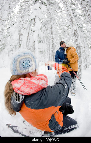 Un adulto metà donna e uomo pongono mentre una giovane donna prende le loro foto mentre con le racchette da neve attraverso una coperta di neve foresta. Foto Stock