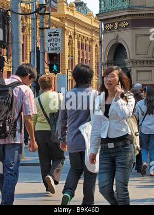 Femmina parlando al cellulare in attraversamento pedonale in Swanston Street con la Flinders Street Melbourne Victoria Australia Foto Stock