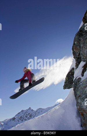 Snowboarder femmina salta fuori da una roccia Foto Stock