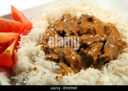 Close-up su di un piatto di carne e funghi stroganoff,sul riso basmati guarnito con pomodoro. Foto Stock