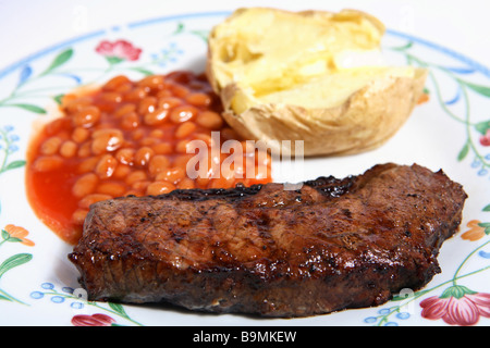 Un brace Lombata di manzo servita su una piastra con fagioli in salsa di pomodoro e patate al forno conditi con burro. Foto Stock