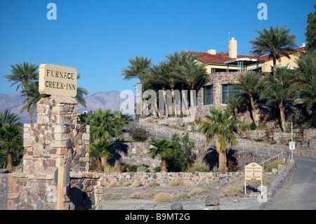 Le terrazze con pareti in pietra dello storico Furnace Creek Inn si innalzano tra lussureggianti palme verdi, affacciate sul vasto e arido pavimento della Death Valley, California. Foto Stock