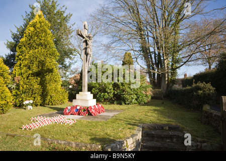 Pirbright Surrey in Inghilterra UK crocifisso di pietra memoriale di guerra con papavero rosso ghirlande e crocifissi nel sagrato della chiesa Foto Stock