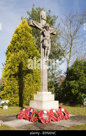 Pirbright Surrey in Inghilterra UK crocifisso di pietra memoriale di guerra con papavero rosso ghirlande in San Michele e tutti gli angeli sagrato Foto Stock