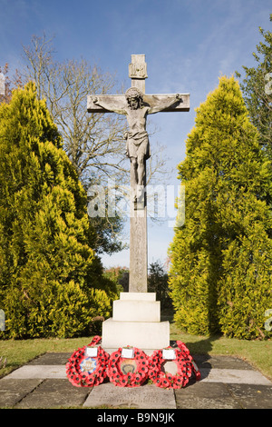 Pirbright Surrey in Inghilterra UK crocifisso di pietra memoriale di guerra con papavero rosso ghirlande in St Michael's sagrato Foto Stock