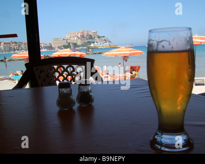 Di fronte al mare, con una birra e sun umberellas e la cittadella in background. Calvi, Corsica, Francia. Foto Stock