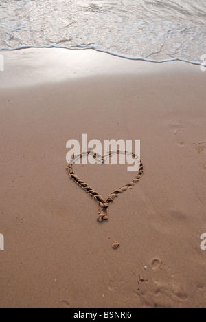 Cuore disegnato nella sabbia bagnata su una spiaggia in prima serata con la marea Foto Stock