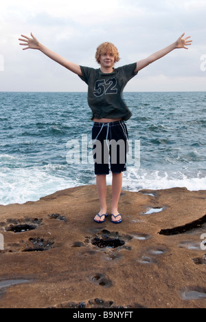 Ragazzo adolescente bracci estesi su una spiaggia di roccia sul ripiano centrale di costa a nord di Sydney Foto Stock