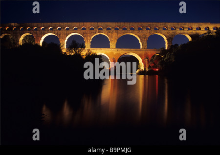 Tempo di notte vista dell'Acquedotto Romano, il Pont du Gard (C1stBC) illuminata di notte e si riflette nel fiume Gard, vicino a Nimes, Francia Foto Stock