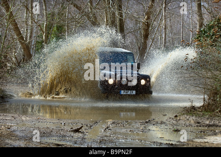 Un Land Rover Defender 90 schizzi attraverso una pista allagata nel Sussex. Foto Stock