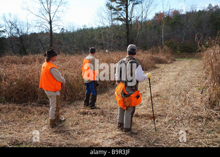 Guida di caccia con due cacciatori nel campo di erba alta giubbotti di arancione Shot guns custodia per il trasporto Foto Stock
