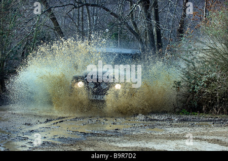 Un Land Rover Defender 90 schizzi attraverso una pista allagata nel Sussex. Foto Stock