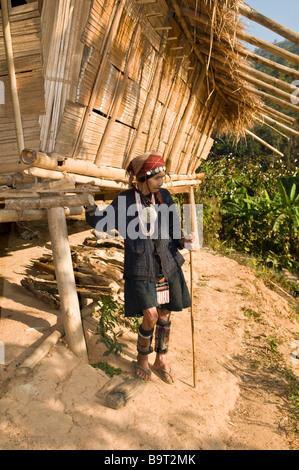 Un Akha donna che indossa un capo tradizionale di indossare abiti e sorge accanto alla sua casa nel suo piccolo villaggio nel nord della Thailandia. Foto Stock