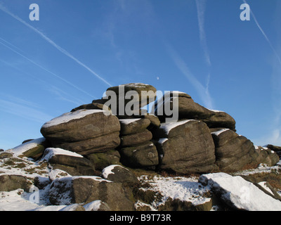 Parzialmente coperta di neve gritstone tor contro un cielo blu con jet sentieri e quasi la luna piena Foto Stock