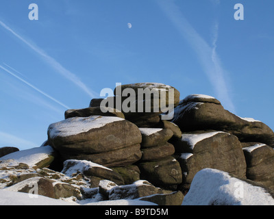 Parzialmente coperto di neve e massi gritstone contro un cielo blu con jet sentieri e quasi la luna piena Foto Stock