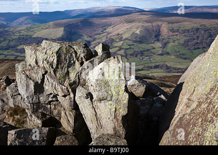 Licheni crescono su vecchio rosso rocce di arenaria sulla cima della montagna di Sugarloaf con il nero montagne in distanza Wales UK Foto Stock