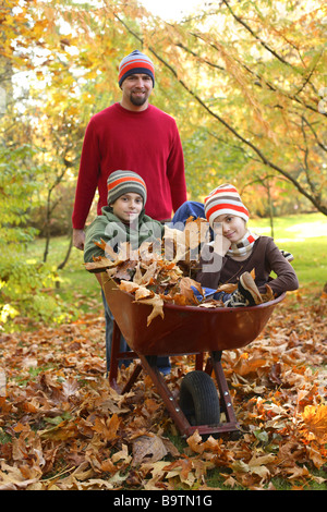 Padre con i bambini e la caduta di foglie in carriola Foto Stock