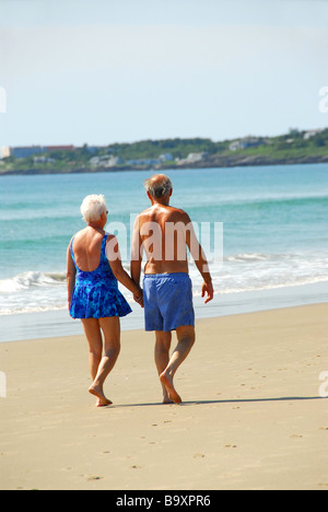 Felice coppia in pensione facendo una passeggiata su una spiaggia tenendo le mani Foto Stock