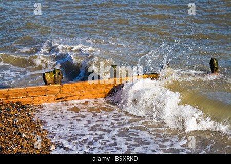 Ondata di schiantarsi su una struttura di frangionde su di una spiaggia di ciottoli. Foto Stock