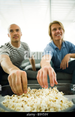 Due uomini seduti sul divano mangiare popcorn Foto Stock
