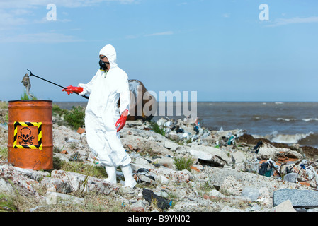 Persona in tuta protettiva mettendo i pesci morti in rifiuti pericolosi canna Foto Stock