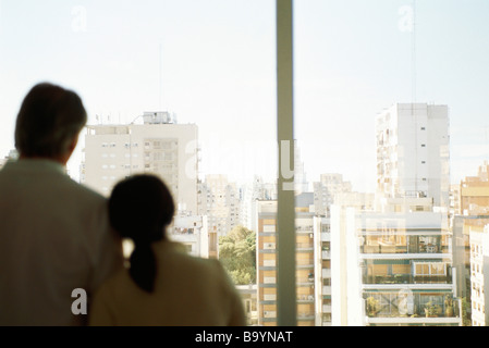 Giovane, testa di donna uomo sulla spalla, insieme alla finestra guardando vista città Foto Stock