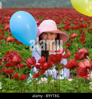 Ragazza giovane con un cappello e il blu mongolfiere in un rosso di campo dei fiori Foto Stock