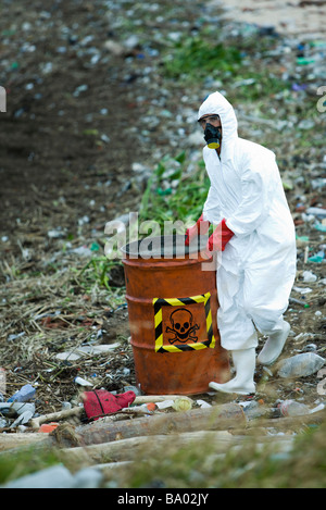 Persona in tuta protettiva che trasportano barile di rifiuti pericolosi Foto Stock