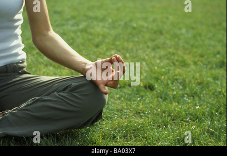Donna seduta nella posizione del loto sull'erba, ritagliato Foto Stock