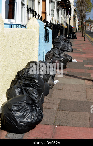 Una linea di nero bin liner di aspettare di essere raccolti dal bin gli uomini sulla raccolta differenziata dei rifiuti al giorno Foto Stock