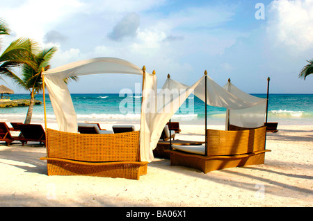 Sedie a sdraio e tettoie su una spiaggia tropicale con una bella sabbia bianca, blu verde acqua e le onde del mare. Foto Stock