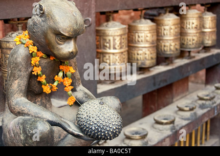 Ottone monkey accanto a ruote della preghiera presso il Tempio Dorato in Patan Nepal Foto Stock