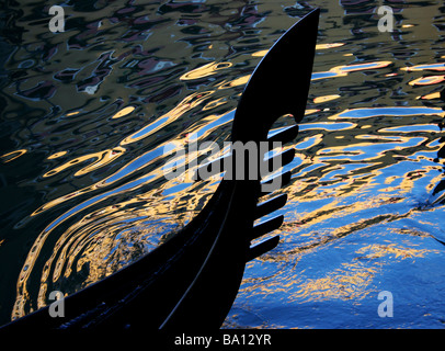 Ferro di gondola silhouette con riflessi blu e giallo colorati e. Riples nel canale acqua Venezia Italia Foto Stock