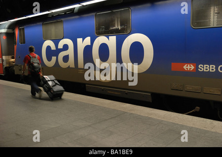 Un passeggero tirando un sacco wheely sulla piattaforma del treno sotto l'aeroporto di Zurigo in Svizzera come un treno merci va passato Foto Stock