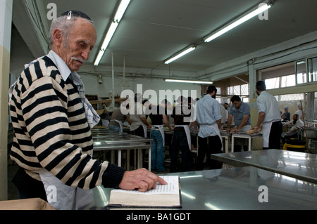 Un ebreo religioso prega mentre altri ebrei preparano Matzot tradizionale Pane azzimo mangiato durante la Pasqua al panificio Kfar Chabad Israele centrale Foto Stock