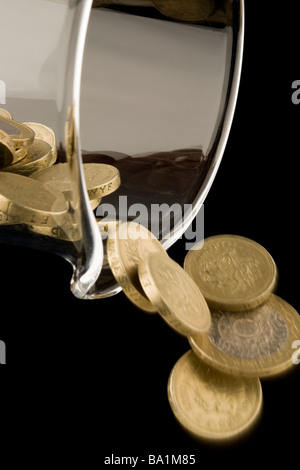 Una libbra e due monete sterlina versando fuori da una caraffa di vetro Foto Stock