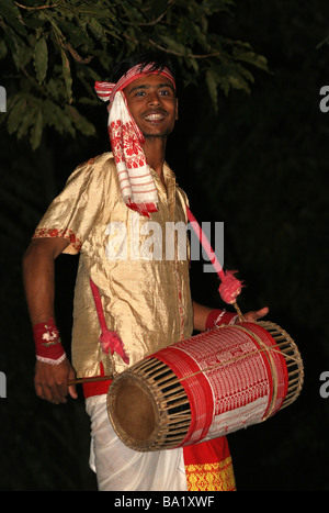 Assamese uomo in abito tradizionale Riproduzione di un tamburo Dhol come parte di un Bihu Dhol balli di gruppo Foto Stock