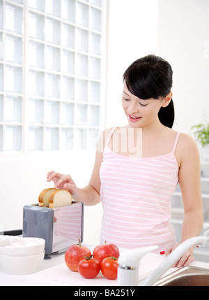 Giovane donna mettendo fette di pane tostato in un tostapane elettrico da parte di pomodori Foto Stock