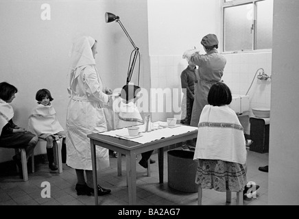 1950s, i bambini con tovaglioli da tè sulle spalle aspettano a loro volta per far ispezionare i capelli per pidocchi o nit dall'infermiera locale del distretto, Inghilterra, Regno Unito Foto Stock