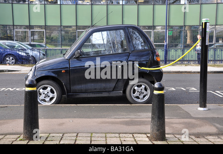 Auto elettrica essendo caricato con un cavo inserito in uno spazio di parcheggio Foto Stock