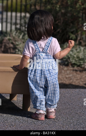 Asian American 18 mese vecchia ragazza in piedi alla base di una slitta nell'area bambini di un parco pubblico a San Jose, CA. Foto Stock