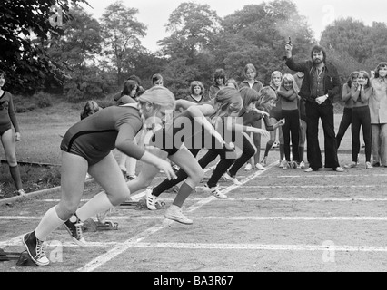 Negli anni settanta, foto in bianco e nero, di edificazione, Scuola, Sport, educazione fisica, palestra classe, via racing, sprint, start, giovani ragazze a partire, di età compresa tra i 10 e i 12 anni, sport insegnante fornisce il segnale di partenza da una pistola di avviamento Foto Stock