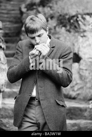 Sechziger Jahre, Menschen, Gesundheit, junger Mann zuendet sich eine Zigarette un Foto Stock