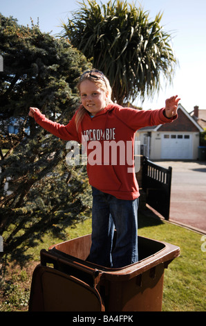 Giovani 9 yr old girl salta in alto e in basso in un giardino del consiglio il riciclo bidone dei rifiuti REGNO UNITO Foto Stock