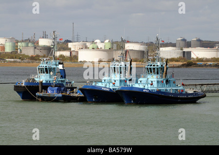 Tre ocean andando rimorchiatori su Southampton acqua con uno sfondo della raffineria di Fawley serbatoi di stoccaggio Foto Stock