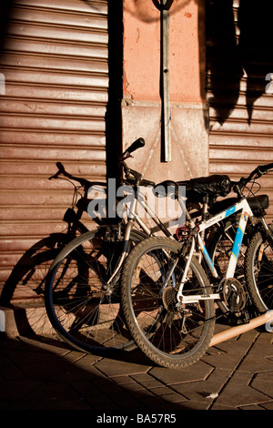 Bassa sera sun gettando ombre su biciclette appoggiata contro le serrande di un mercato in stallo i souk di Marrakech, Marocco Foto Stock