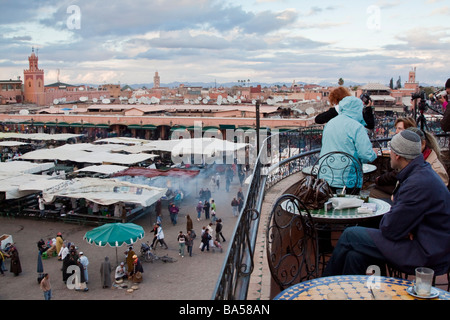 I turisti rilassarsi bevendo tè alla menta da una caffetteria con terrazza sul tetto che si affaccia sulla piazza Jemaa el Fna nella Medina di Marrakech Foto Stock